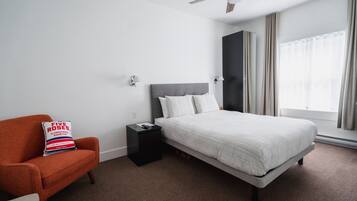 Habitación de hotel con cama, mesita de noche, una silla y ventilador de techo.