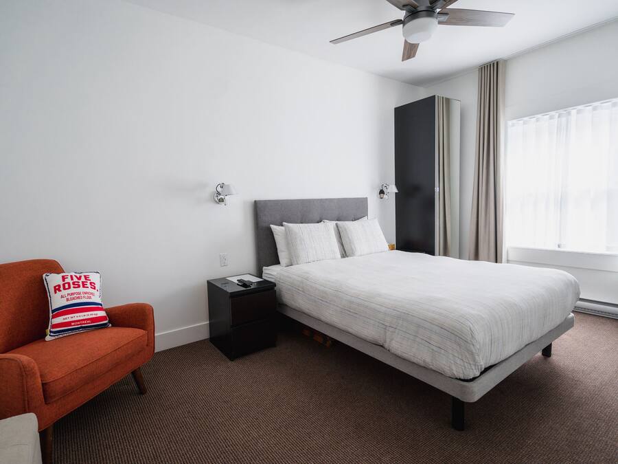 Habitación de hotel con cama, mesita de noche, una silla y ventilador de techo.