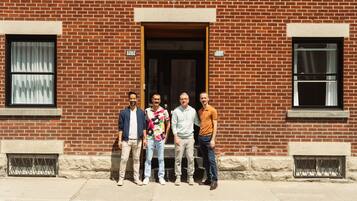 A group of five men standing in front of a brick building with numbered windows and a door.