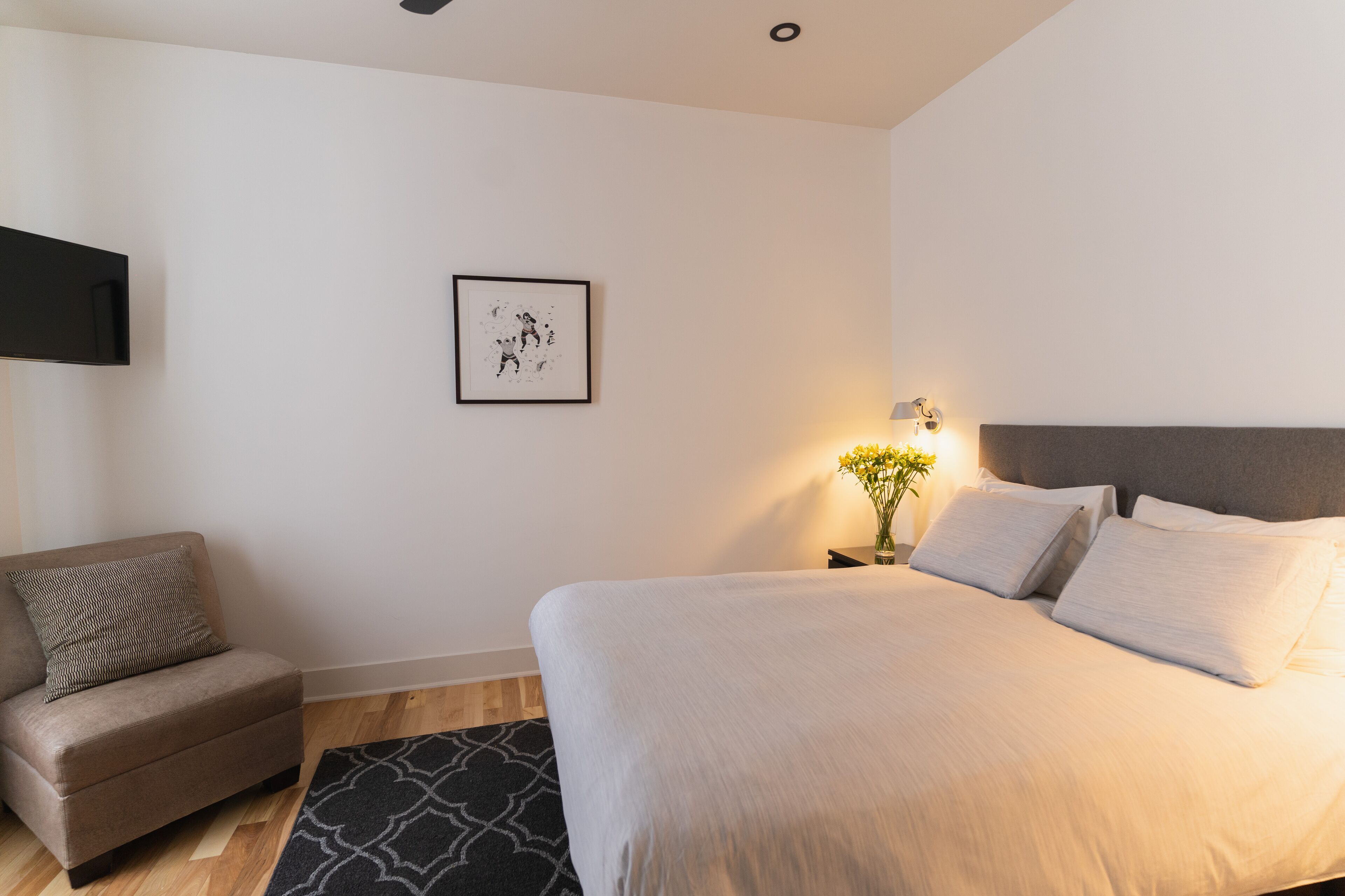 A bedroom with a bed, a chair, a framed picture, and a nightstand with a lamp.