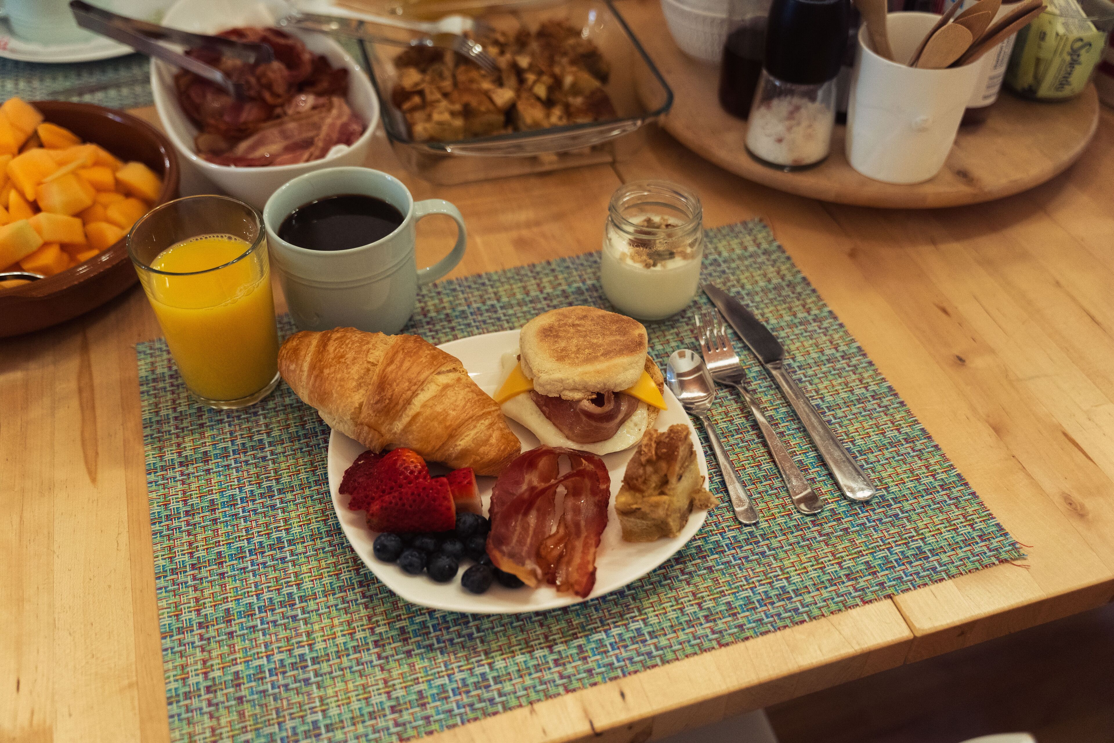 A breakfast table with croissants, a sandwich, strawberries, blueberries, and a glass of orange juice.