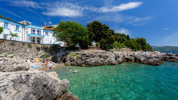 A coastal hotel with clear turquoise waters, rocky cliffs, and lush greenery.