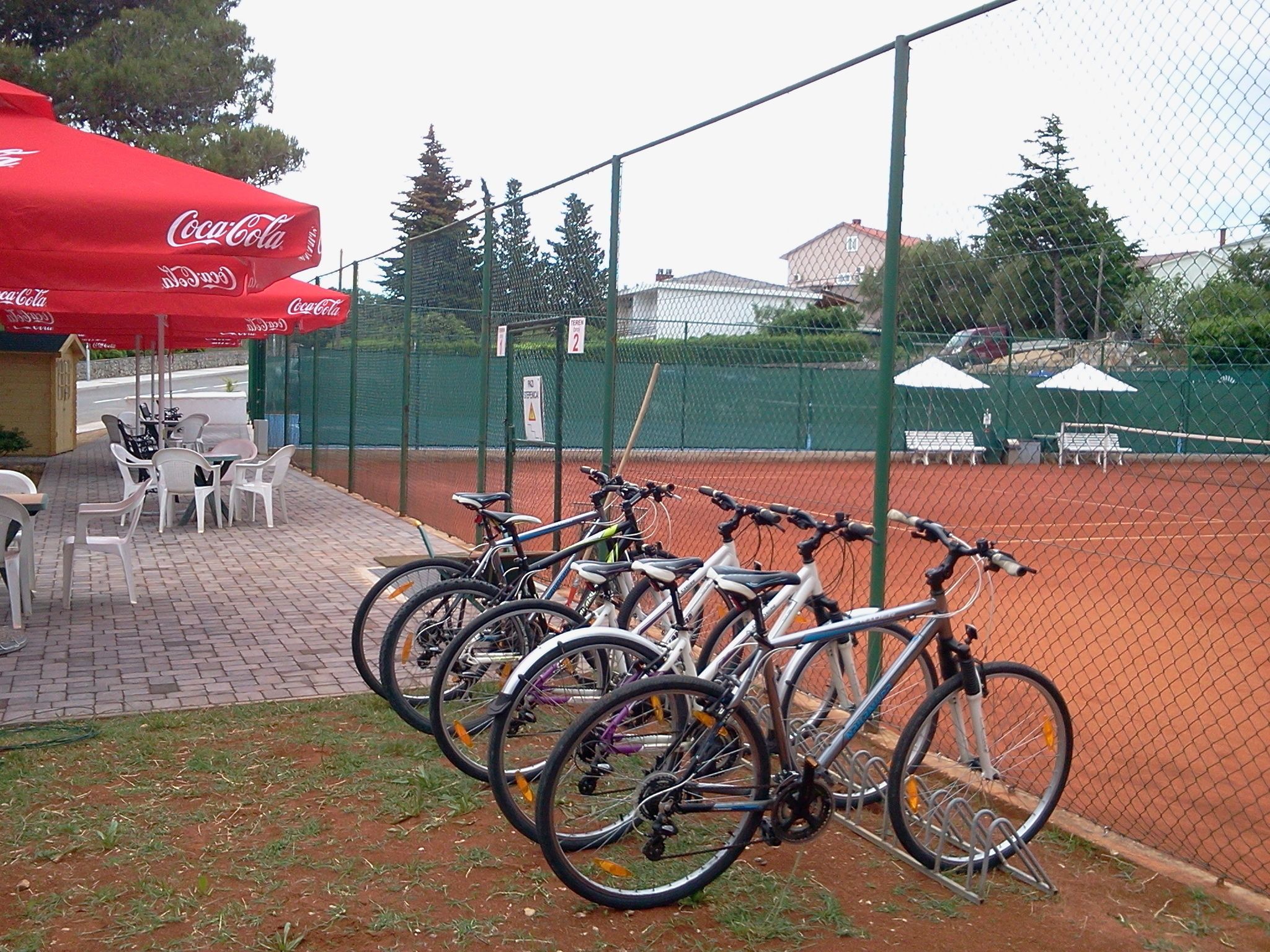 Una cancha de tenis con bicicletas estacionadas en el frente, rodeada por una cerca.