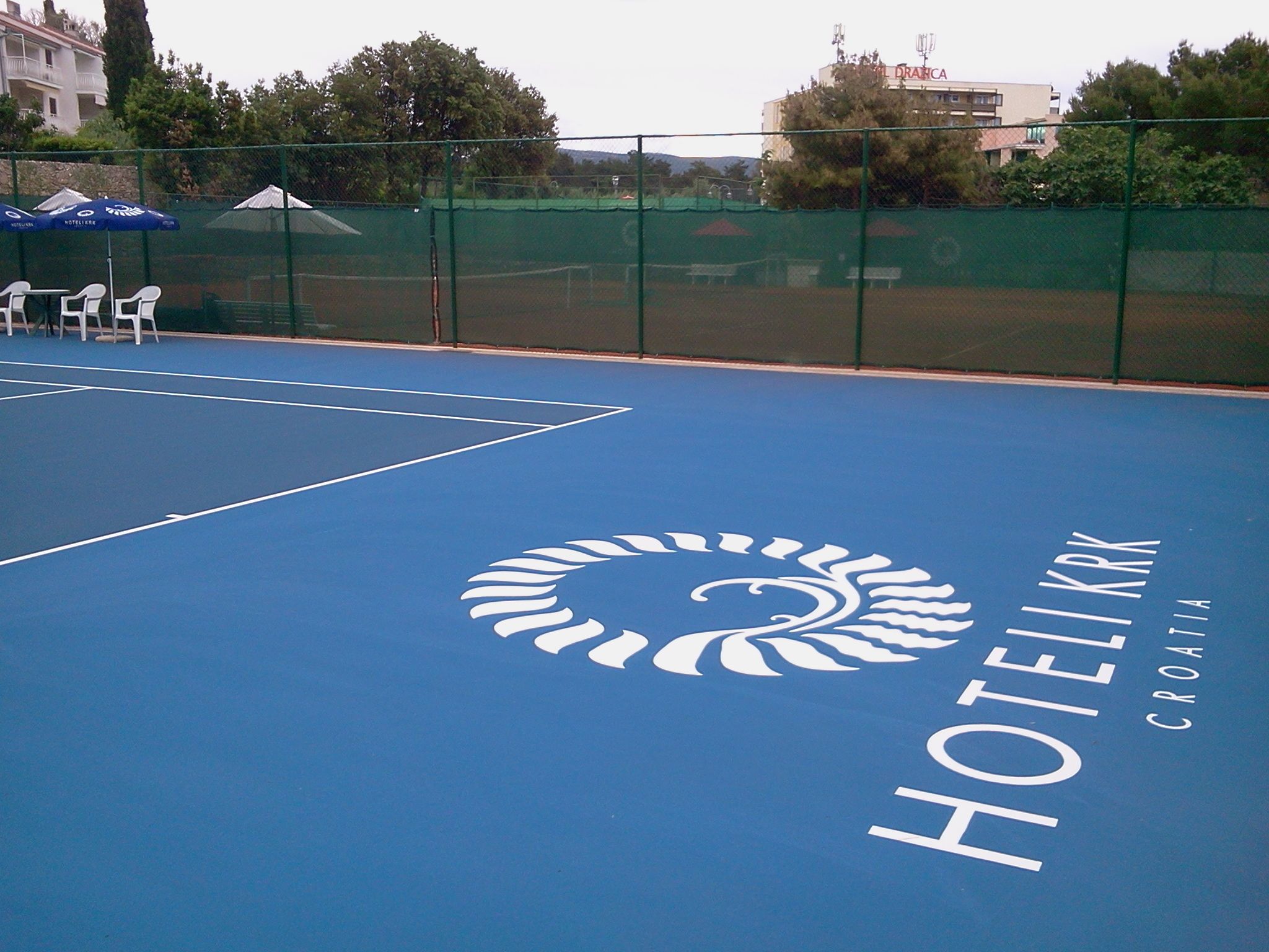 Ein blauer Tennisplatz mit einem Logo und der Aufschrift 'HOTEL KRK CROATIA'.