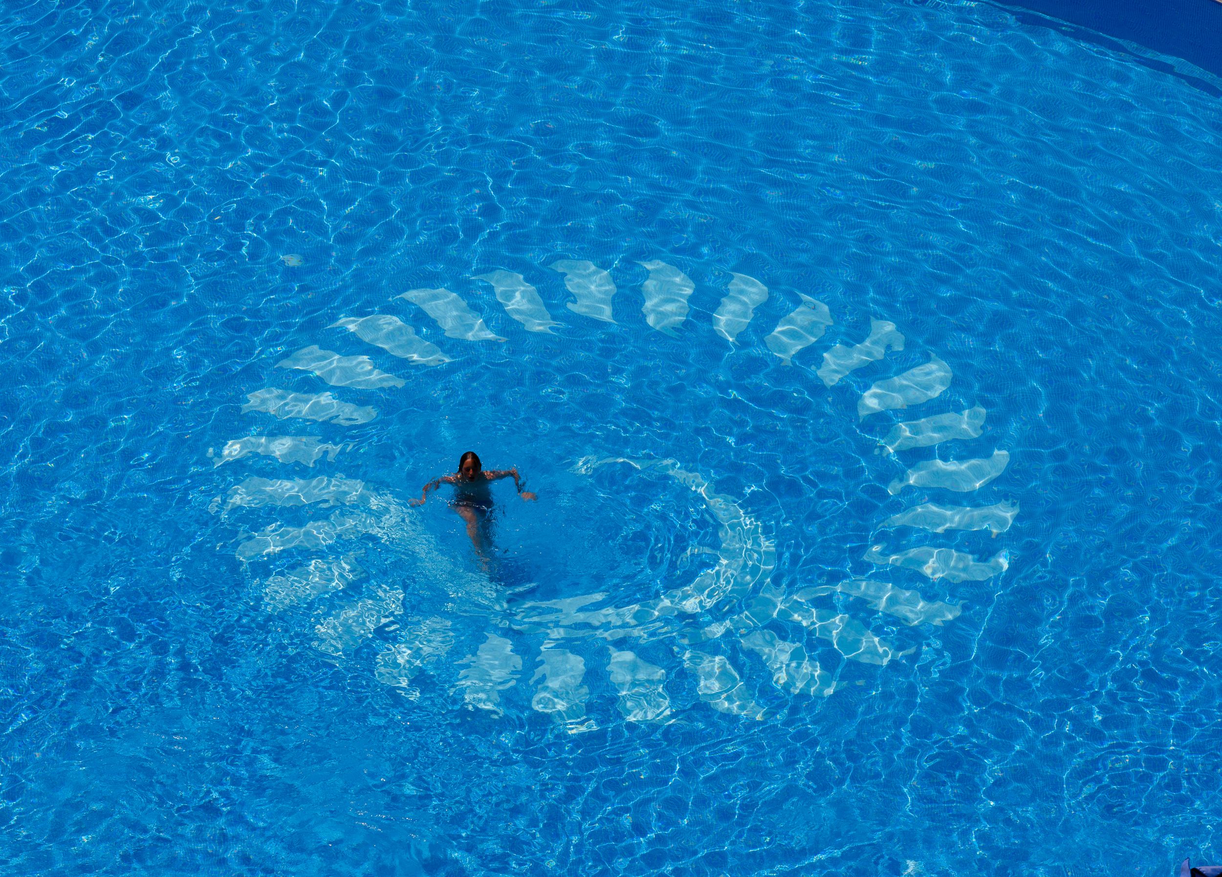 Una persona nada en una piscina azul cristalina con un patrón circular en la superficie del agua.