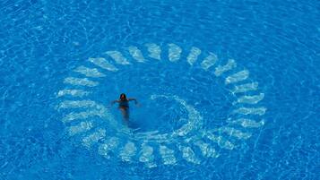 Una persona nada en una piscina azul cristalina con un patrón circular en la superficie del agua.