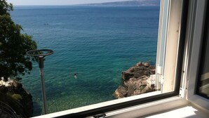 A view of the sea from a window, with clear water and a rocky coastline.