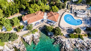 An aerial view of a resort with a swimming pool, multiple buildings, and rocky terrain.