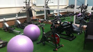 Un gimnasio con equipo de ejercicio, pelotas grandes y suelo verde.
