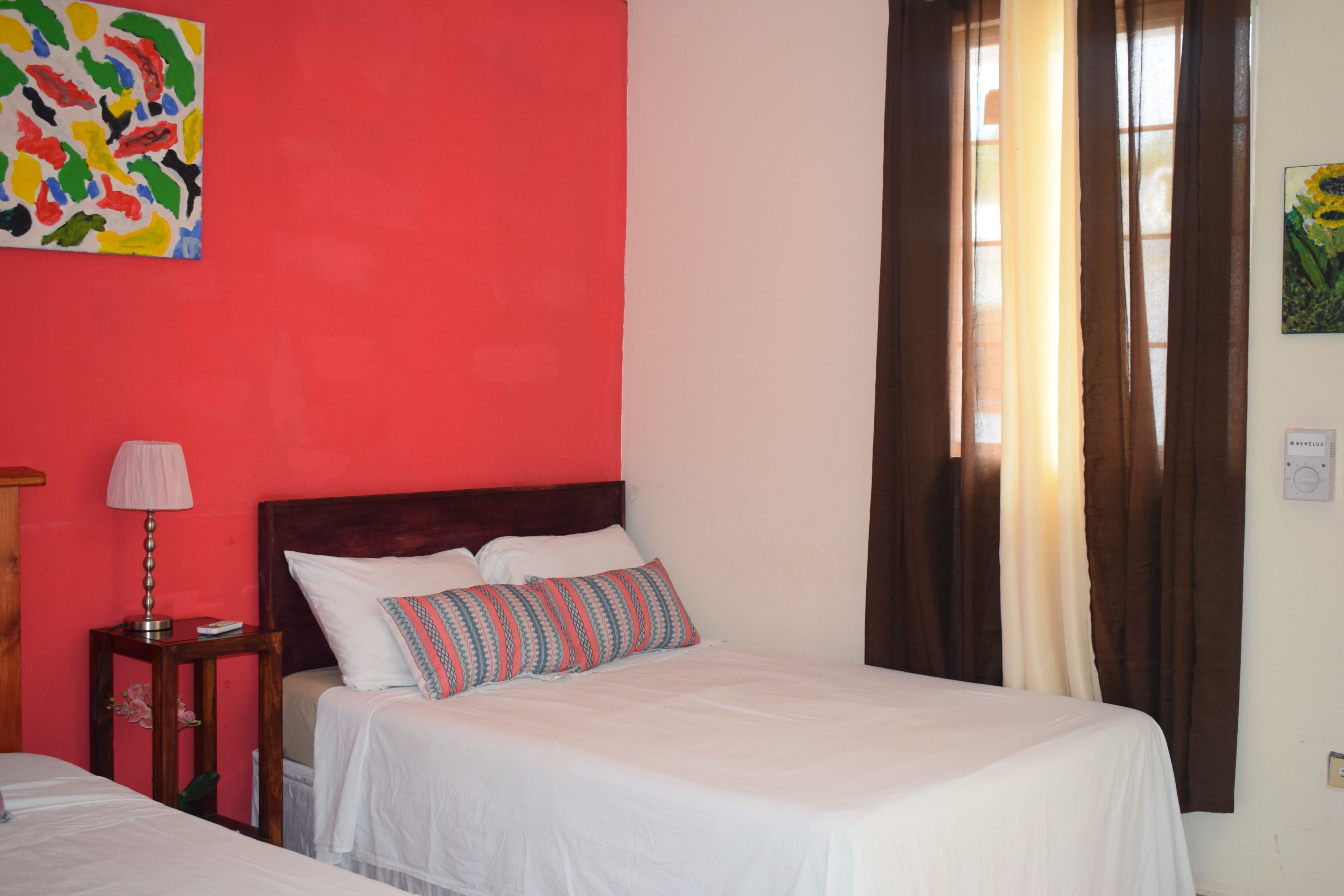 A hotel room with a bed, a nightstand, a lamp, and a colorful abstract painting on the wall.