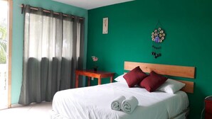 Un dormitorio con una cama, cabecera de madera, una mesita con un florero y un adorno en la pared.