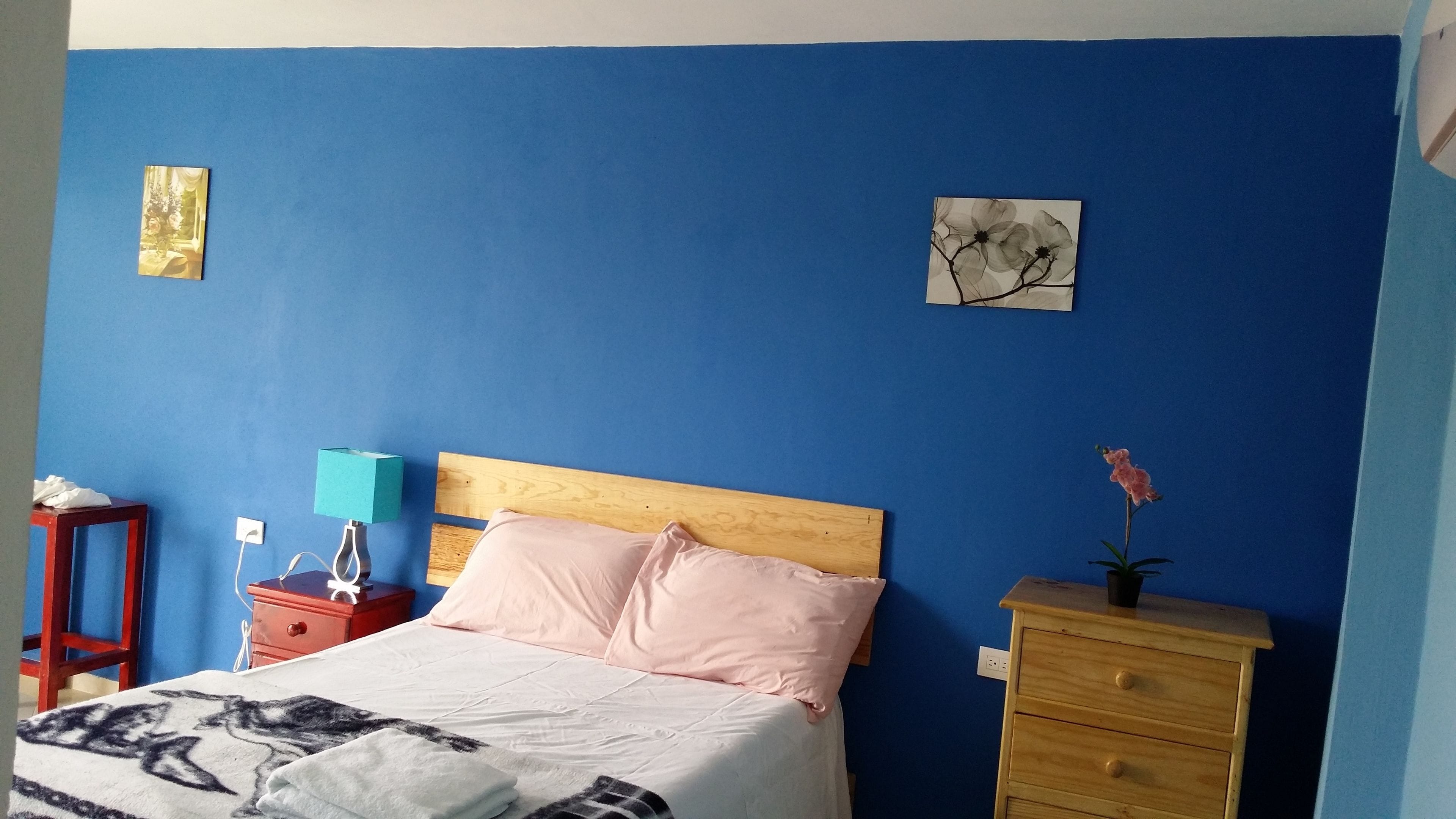 Et soveværelse med seng, sengebord, lampe, kommode og to billeder på væggen.