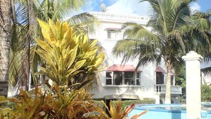 Un edificio blanco con techo rojo, rodeado de palmeras y una piscina.