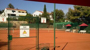 Un court de tennis avec un panneau d’avertissement, des courts numérotés et une banderole Coca-Cola.