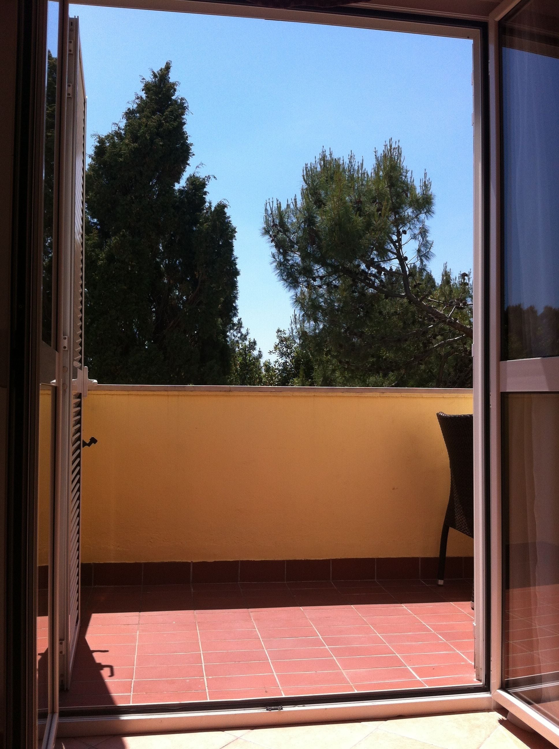 An open sliding door leading to a balcony with a red-tiled floor and a yellow wall.