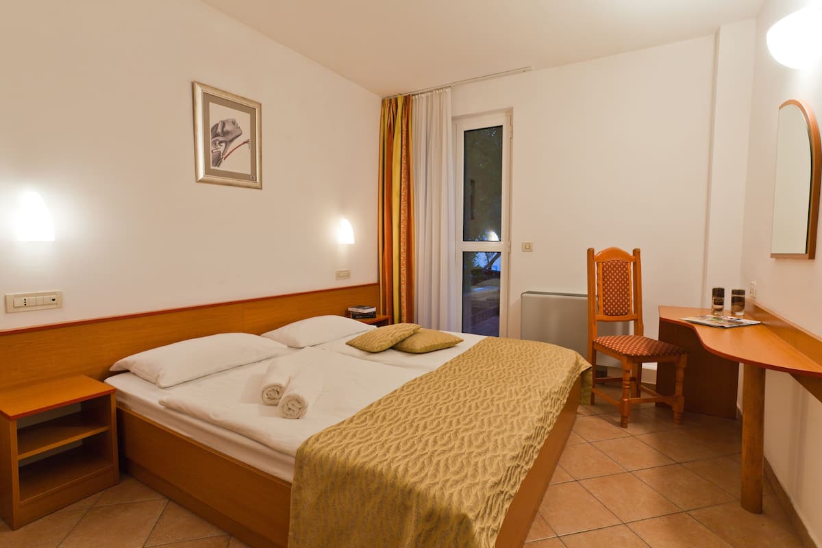 A hotel room with a bed, bedside table, chair, desk, and a window with curtains.