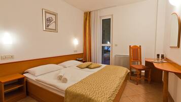 A hotel room with a bed, bedside table, chair, desk, and a window with curtains.