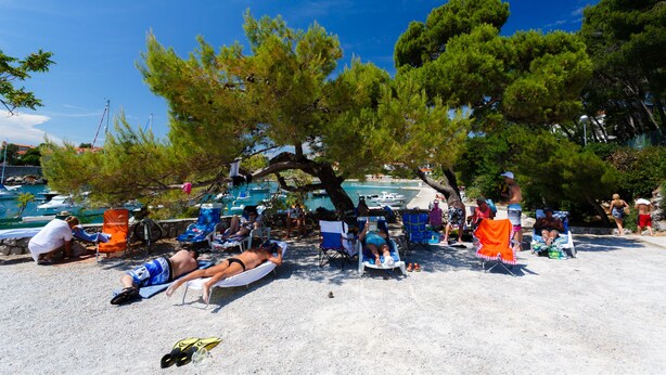 A beach with people sunbathing and swimming, surrounded by trees and boats. - Villa Lovorka - Hotel Resort Drazica (Krk)