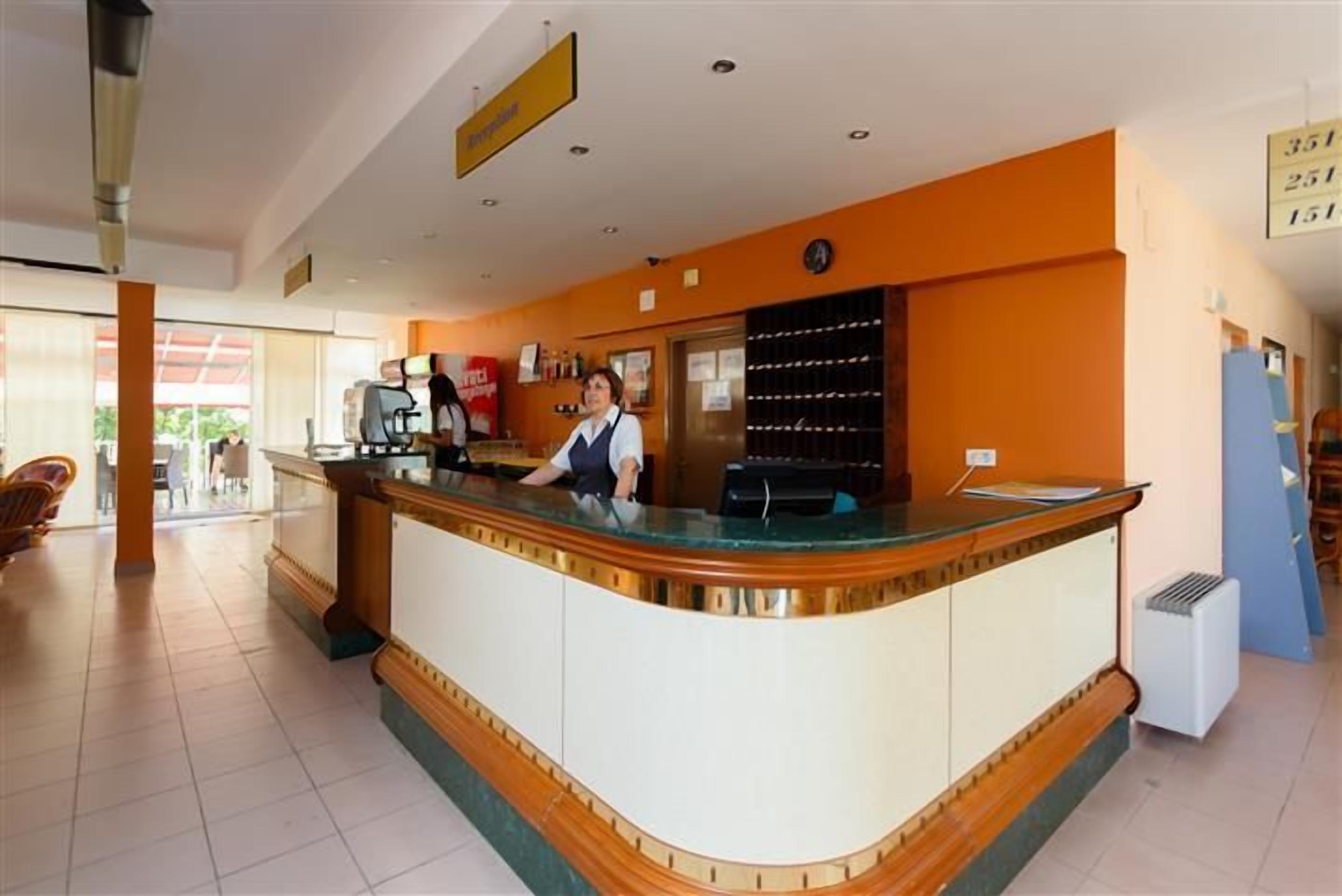 A reception desk with a receptionist, a coffee machine, and a bulletin board.