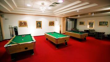 A pool room with three pool tables, red carpet flooring, and framed artwork on the walls.