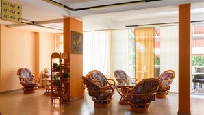 A hotel lobby with wicker chairs arranged around a central table, a plant stand, and a sign indicating room numbers. - Villa Lovorka - Hotel Resort Drazica (Krk)