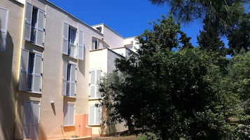 Un edificio de varios pisos con balcones y un árbol en primer plano.