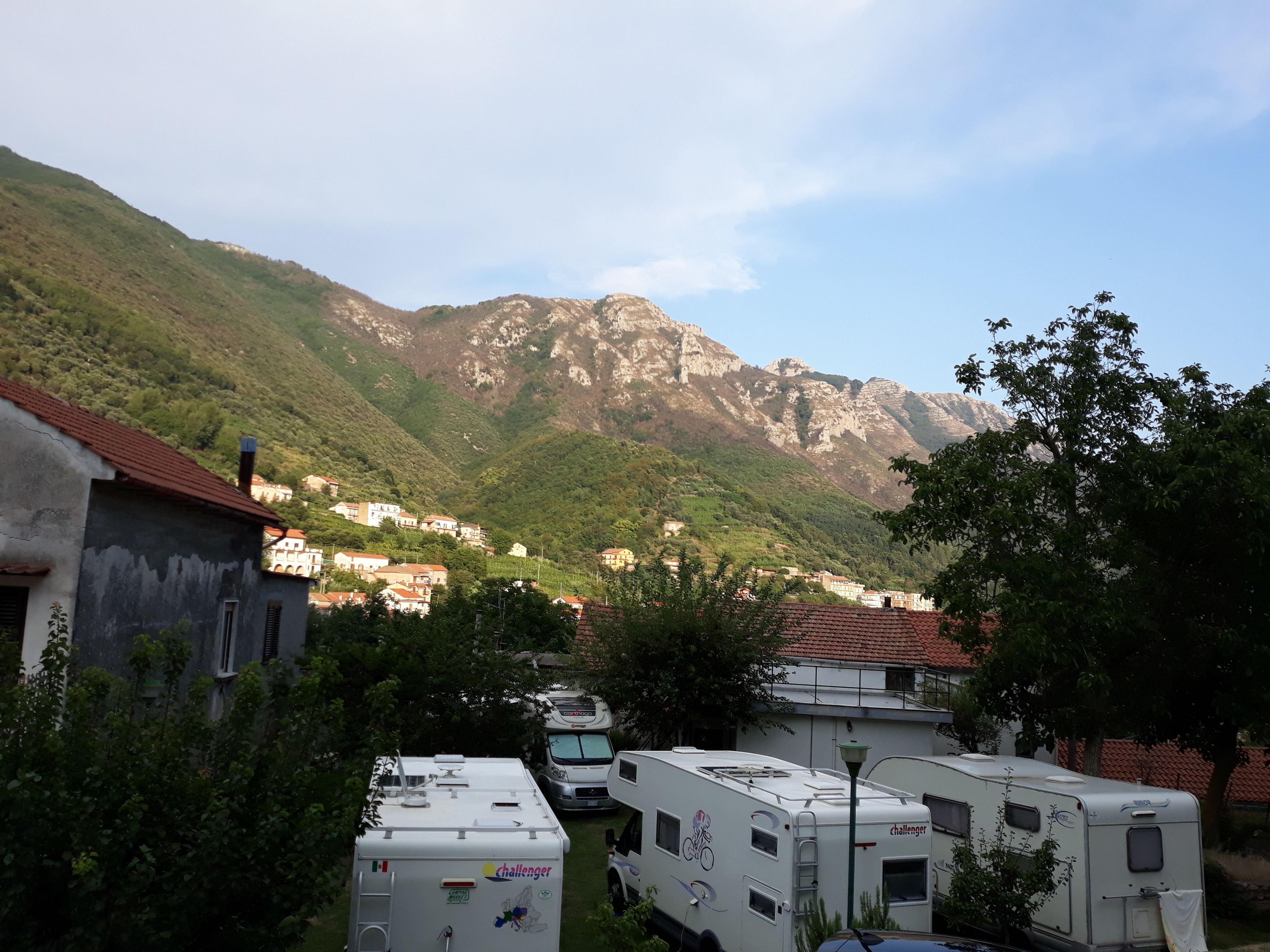 A campsite with RVs parked in a valley, surrounded by mountains and residential buildings.