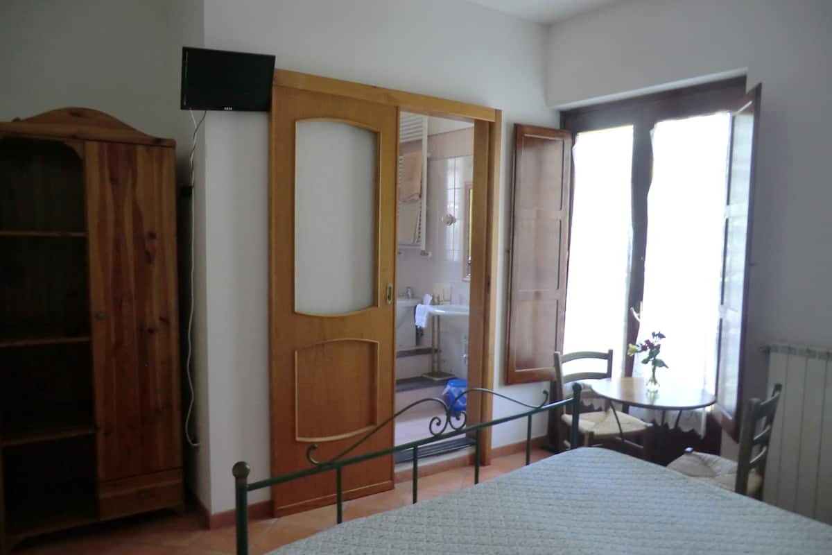 Een kamer met een bed, een houten kledingkast, een aan de muur bevestigde televisie en een badkamer die door een open deur zichtbaar is.