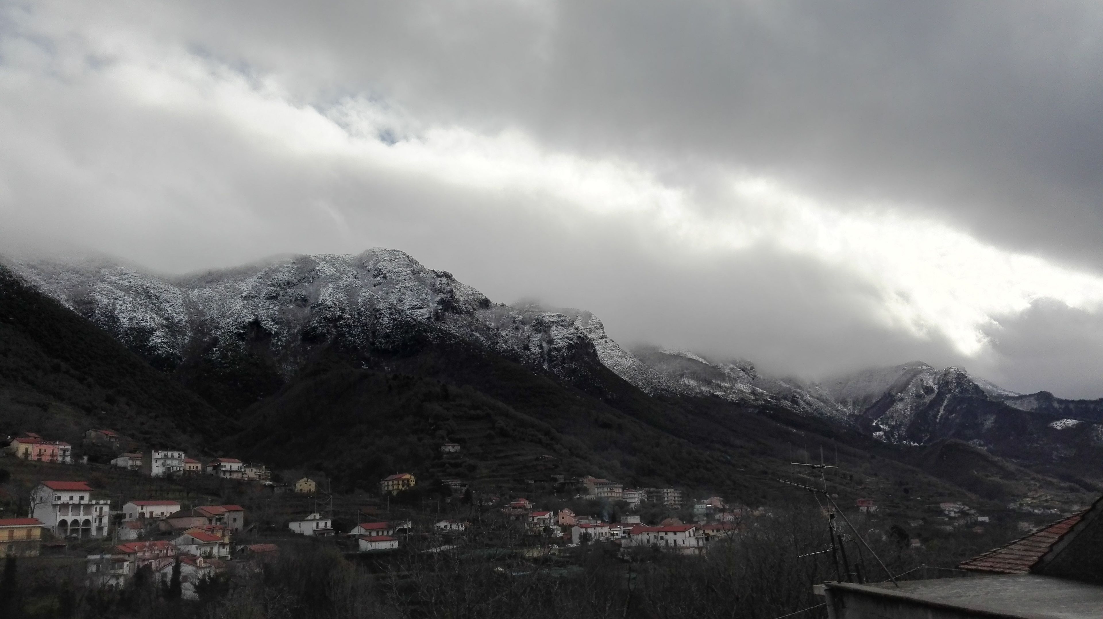 Un paisaje montañoso con picos nevados y un pueblo con edificios de tejados rojos.