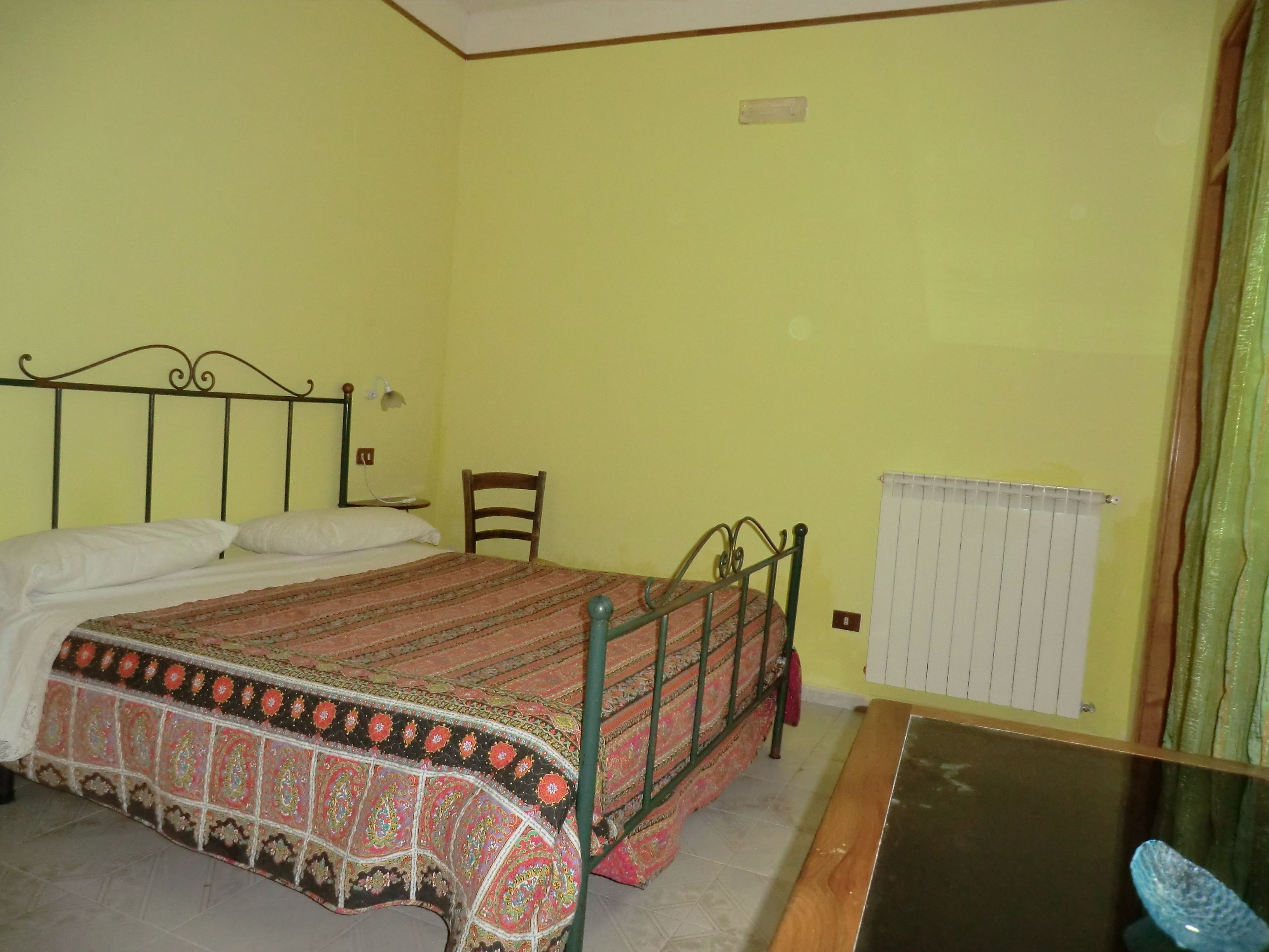 Une chambre avec un lit simple, une chaise, une petite table et un radiateur.