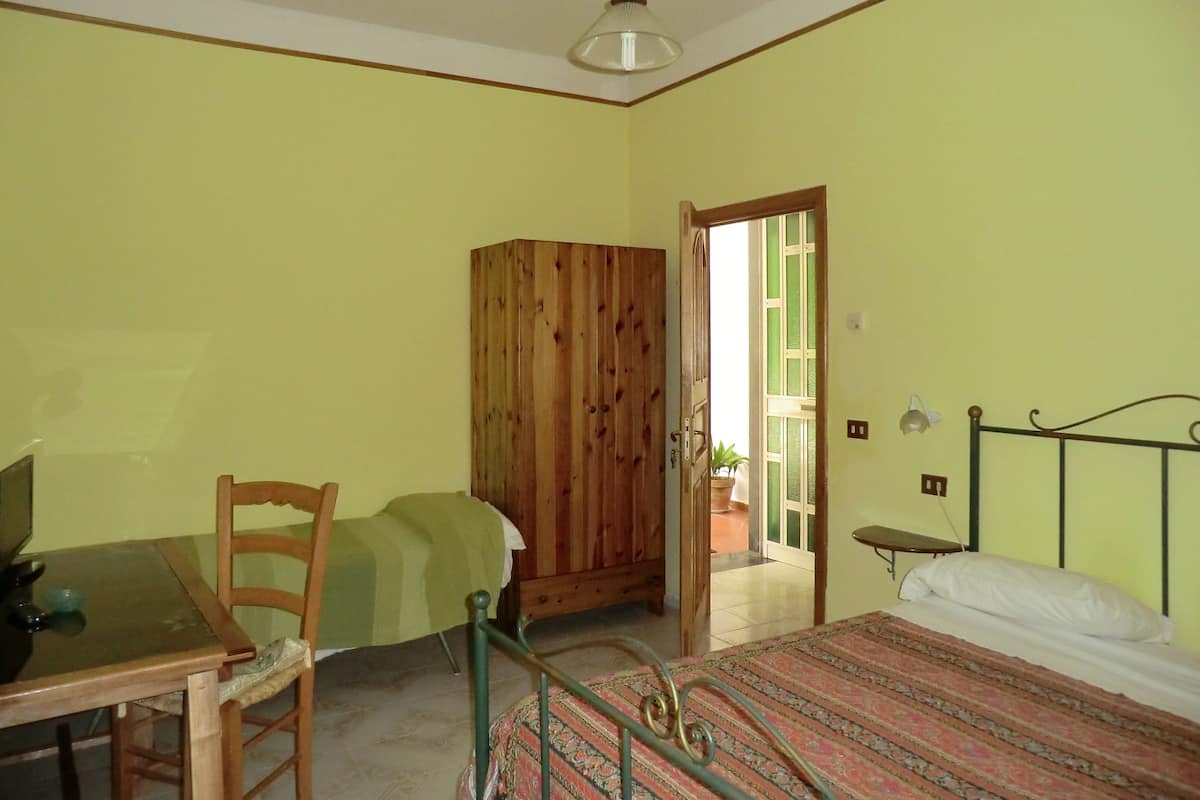 Een kamer met een bed, een houten garderobe, een tafel met stoel en een bijzettafeltje met lamp.