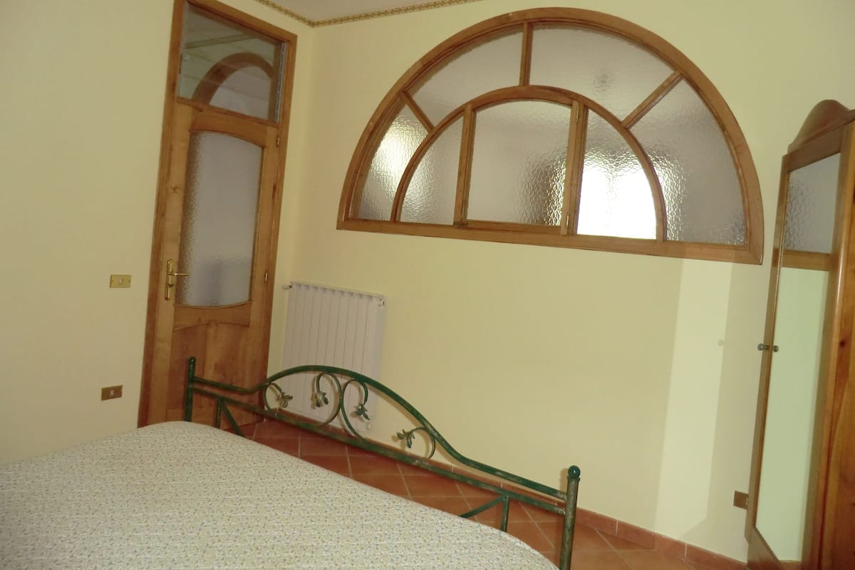Een slaapkamer met een bed, een raam met houten kader en een radiator.