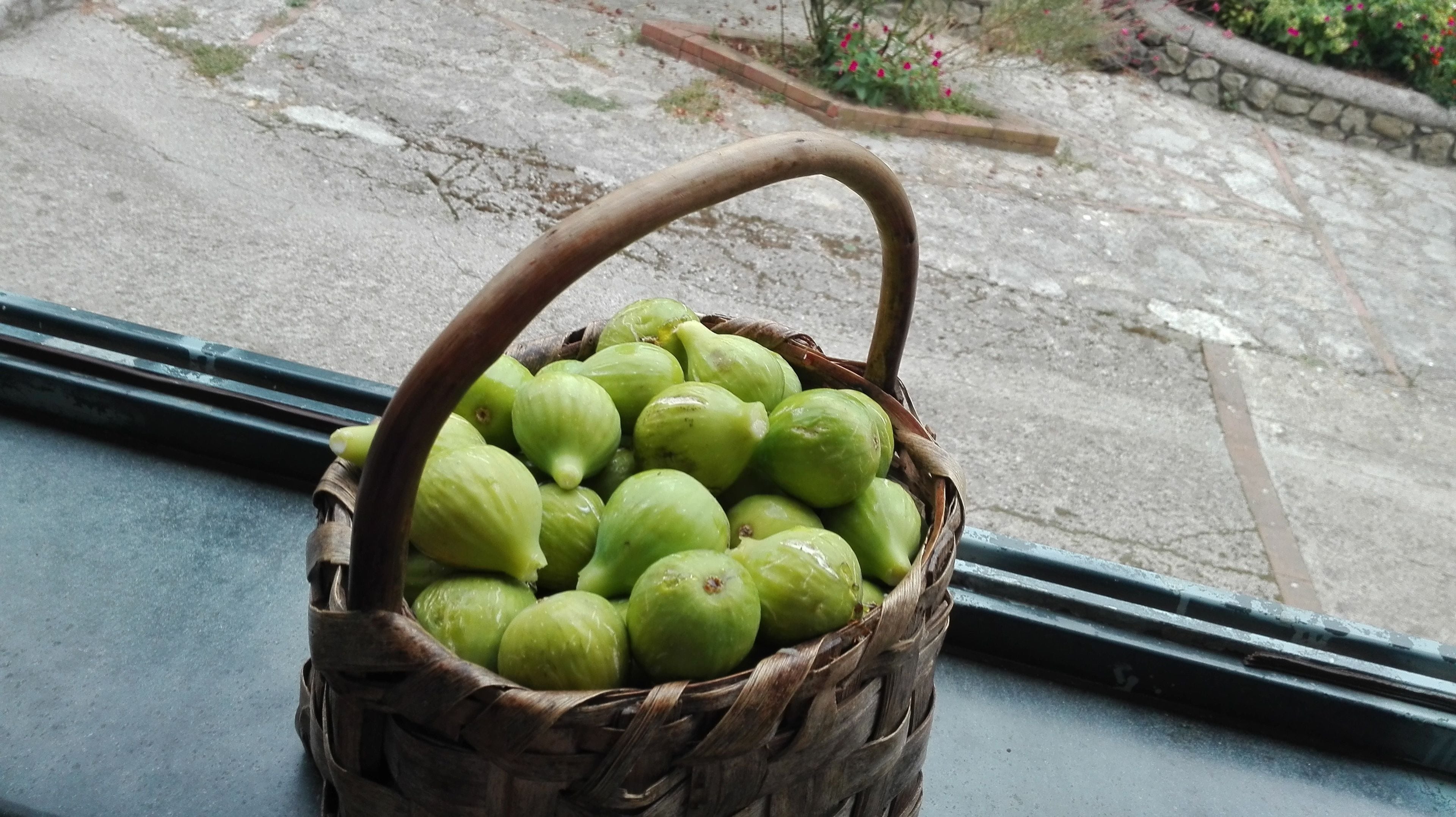Una cesta de mimbre llena de manzanas verdes sobre un alféizar.