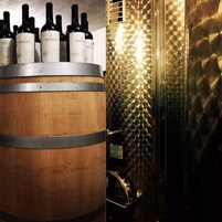 Un barril de madera con varias botellas de vino etiquetadas 'BASILIO' encima.