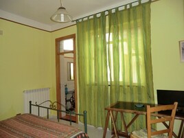 Una habitación con una cama, una mesa y una silla. Hay una ventana con cortinas verdes.