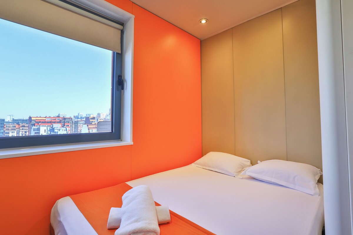 A hotel room with two beds, a large window, and a city view.