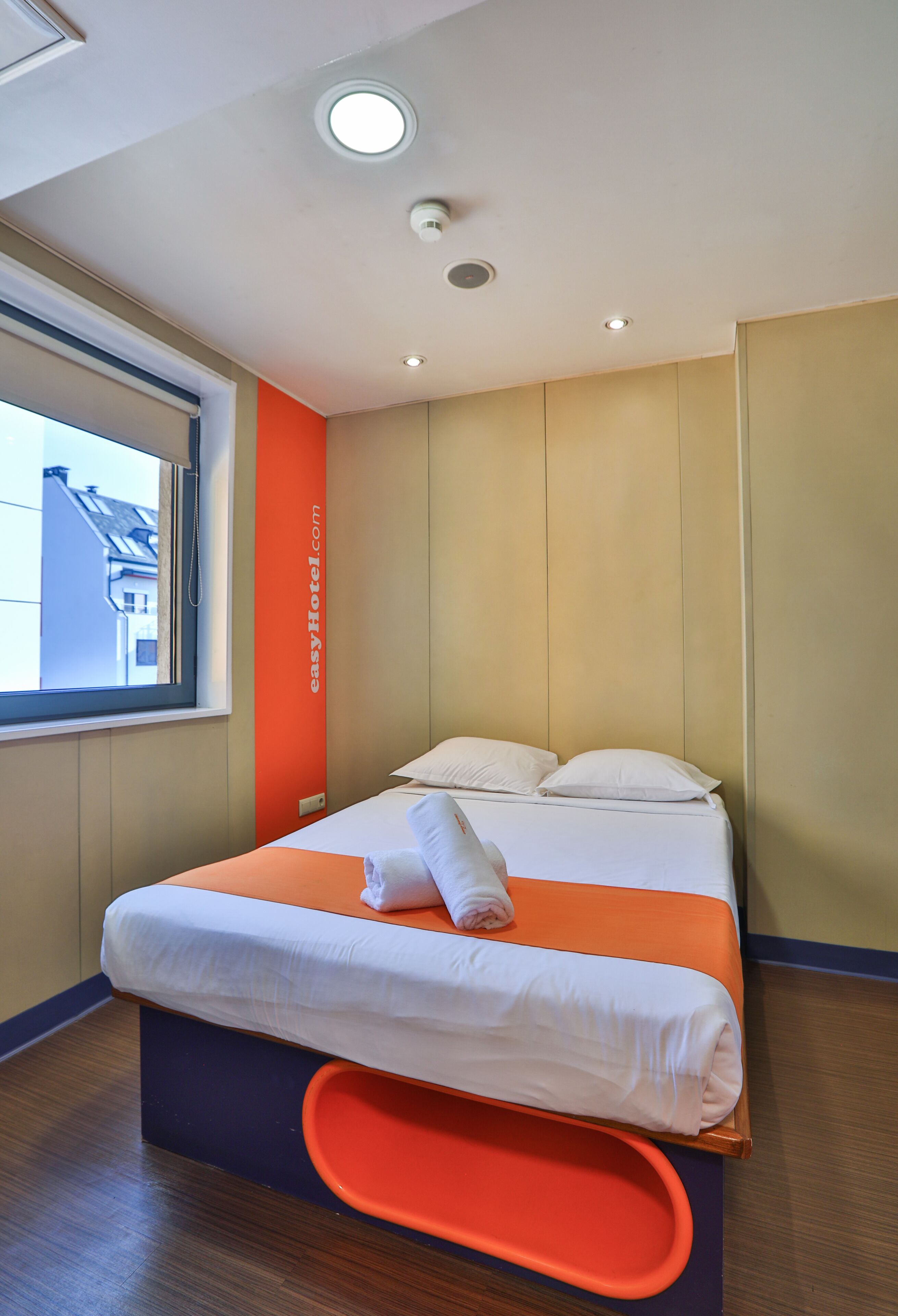 A hotel room with a bed, a window, and a view of buildings outside.