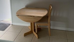 Une pièce avec une table et une chaise en bois, une fenêtre donnant sur un mur de briques et un appareil de climatisation fixé au-dessus de la fenêtre.