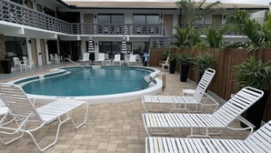 Un espace piscine avec des chaises longues blanches, un sol carrelé et une clôture en bois.