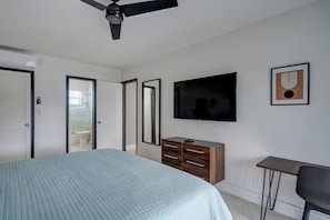 Quarto com cama, televisão, penteadeira e escrivaninha.