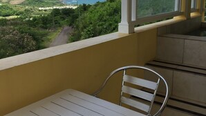 A balcony with a white table and chair, overlooking a scenic view of the ocean and greenery. - South Sea House (Gros Islet)