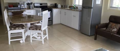 Une cuisine moderne avec des meubles blancs, une table à manger avec des chaises, un réfrigérateur et une fenêtre à barreaux.