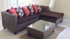 A living room with a brown woven sofa, a glass coffee table, and a large window with a white curtain. - South Sea House (Gros Islet)