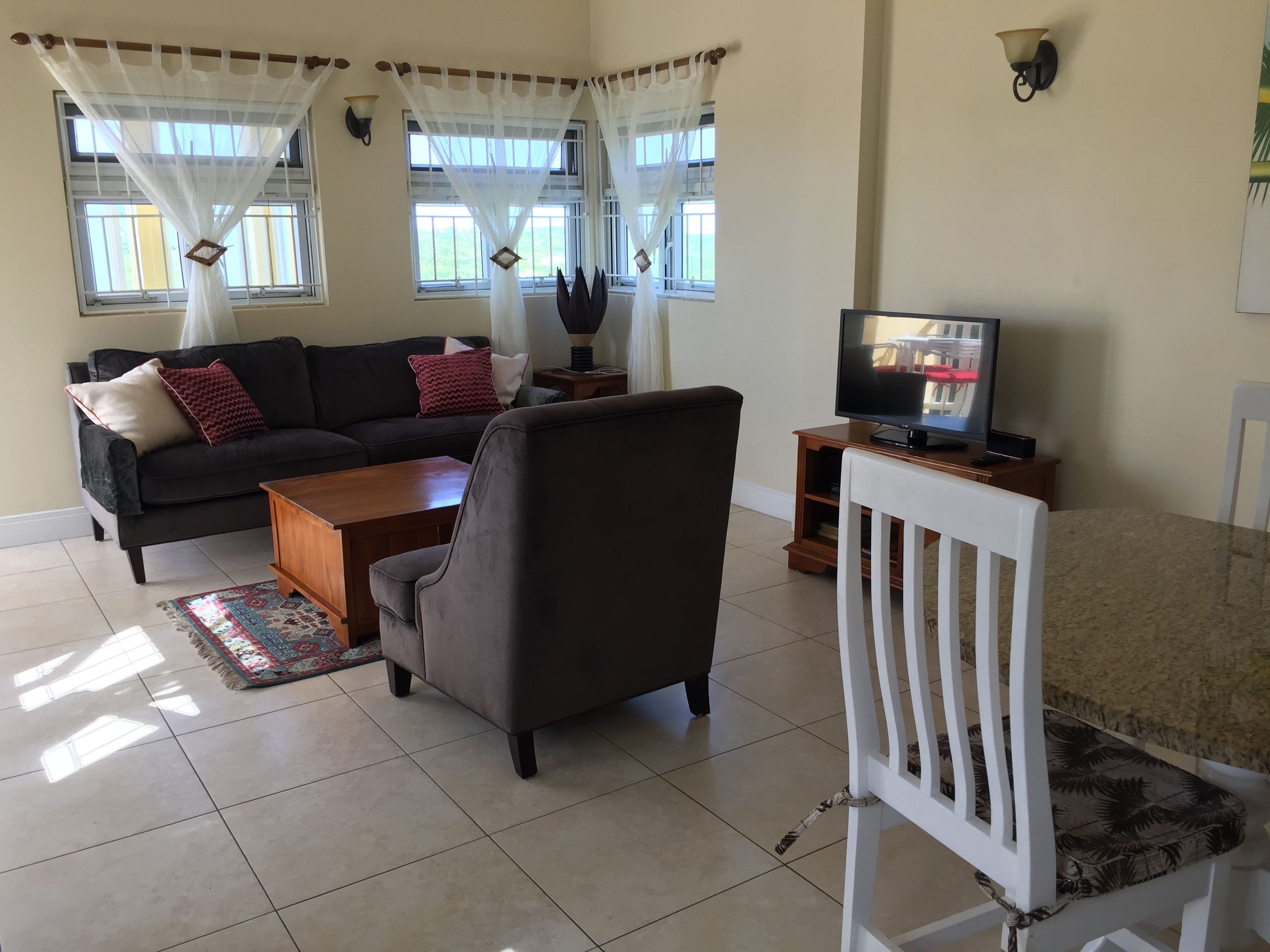 Ein Wohnzimmer mit Sofa, Sessel, Couchtisch, Fernseher und Vorhängen.