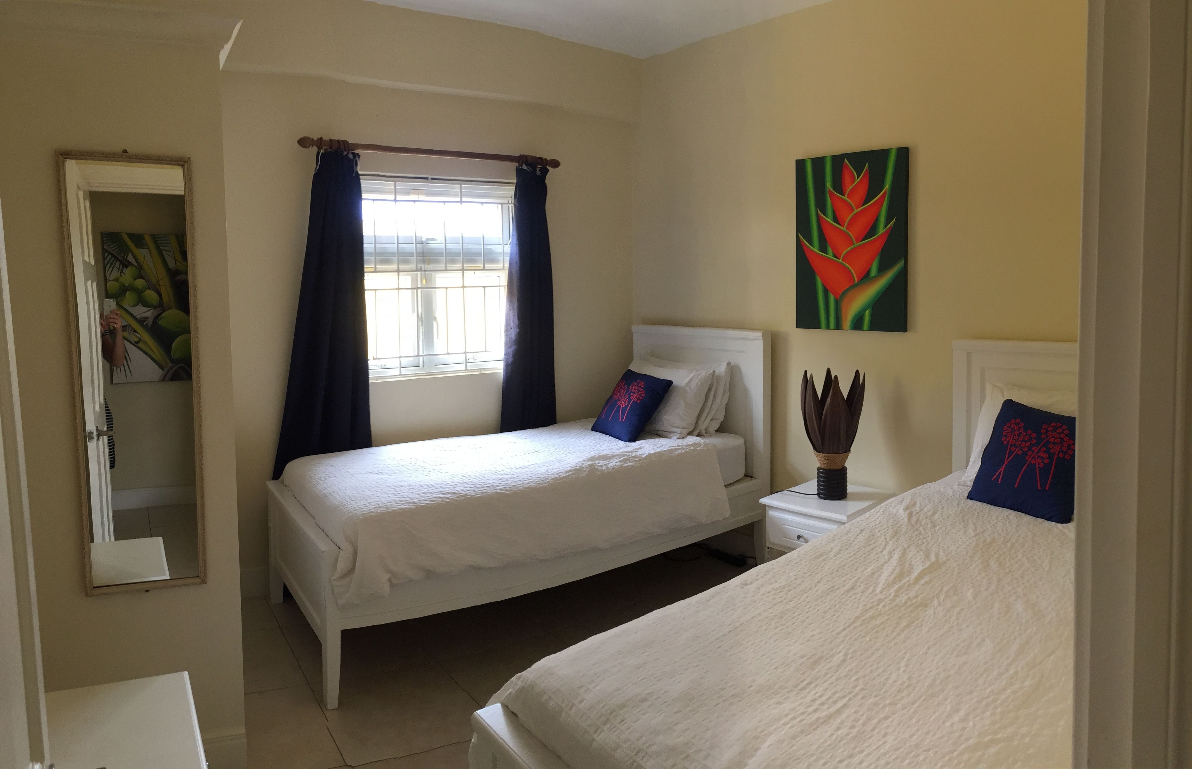 Un dormitorio con dos camas, una ventana con cortinas, un cuadro en la pared y un espejo.