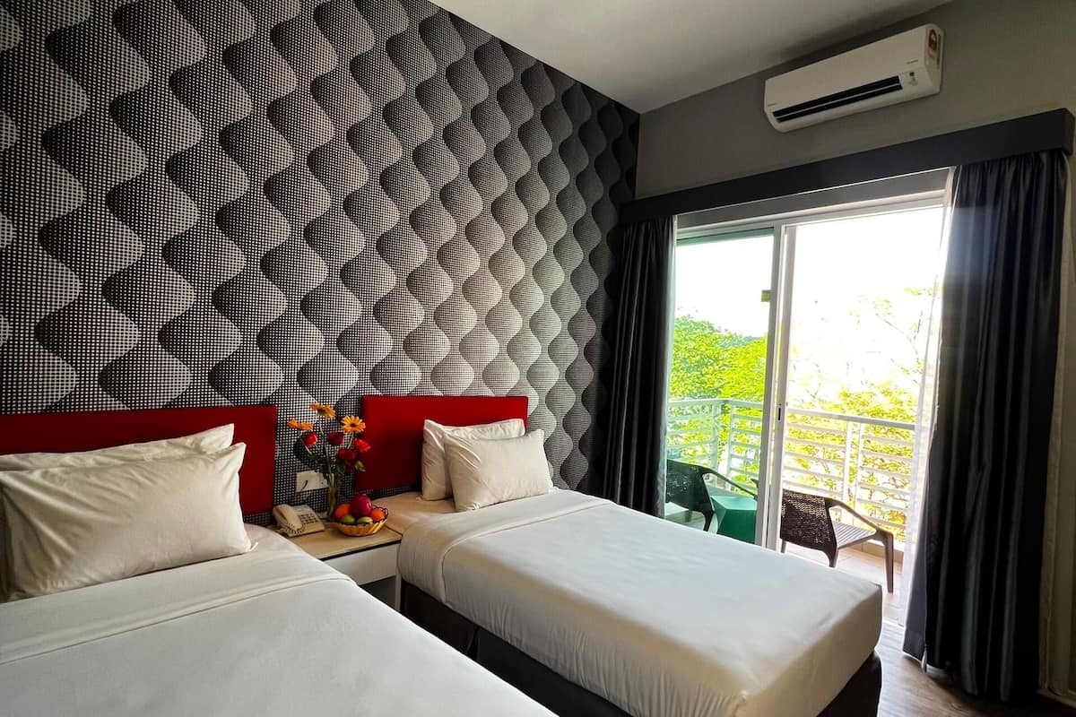 Una habitación de hotel moderna con dos camas, un cabecero rojo, un papel tapiz estampado, un equipo de aire acondicionado y un balcón con vistas.