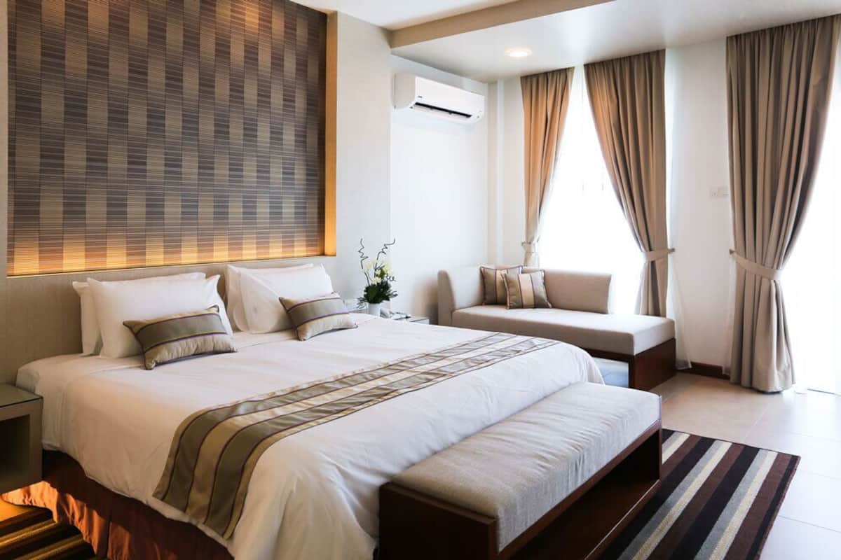 Una habitación de hotel moderna con una cama grande, una mesita de noche, un sofá y una ventana con cortinas.