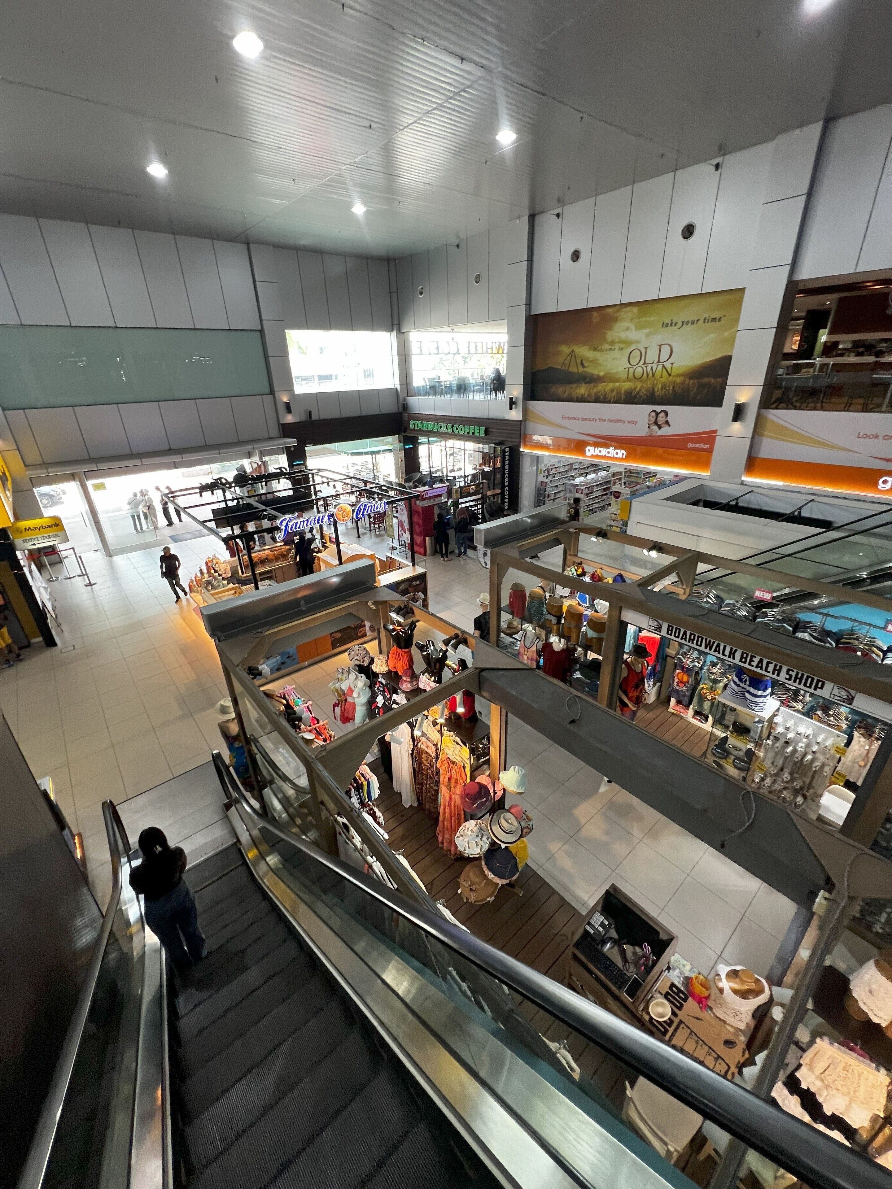 An indoor shopping mall with multiple stores, including a boardwalk beach shop and a Starbucks.