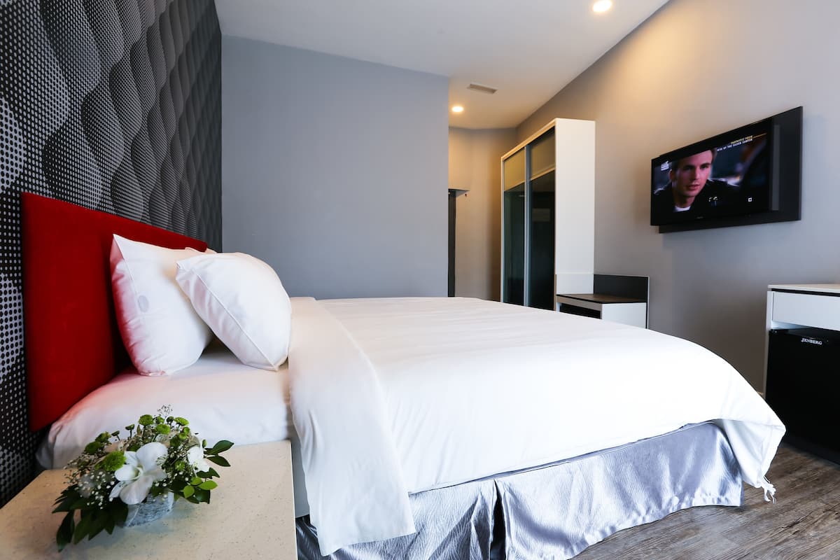 Una habitación de hotel moderna con una cama grande, un televisor de pantalla plana montado en la pared y una mesita de noche con un jarrón de flores.