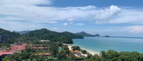 A coastal landscape with a beach, forested hills, and a clear sky.